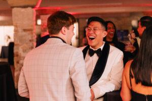 A man in a white tux laughing with another man.