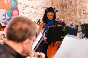 A woman playing cello against a stone background.